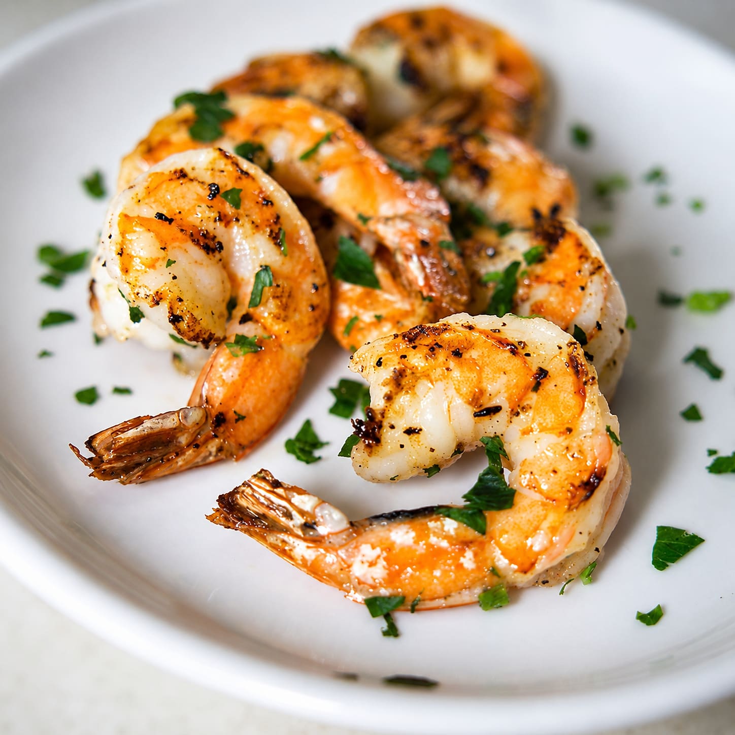 Half a dozen shrimp, sautéed and lightly charred, scattered with parsley on a white plate.